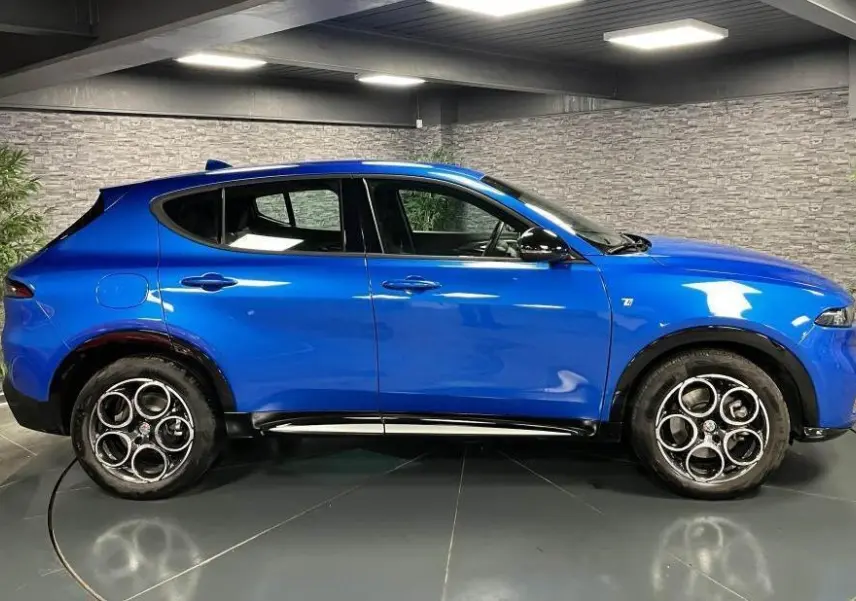 Profil côté gauche de l'Alfa Romeo Tonale 1.5 mHEV 160 TI bleu métallisé avec jantes alliage 18 pouces en intérieur showroom.