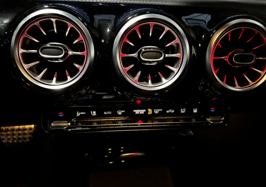Détail intérieur des aérateurs ronds avec éclairage rouge sur tableau de bord noir de la Mercedes CLA 250 e AMG Line 2023.