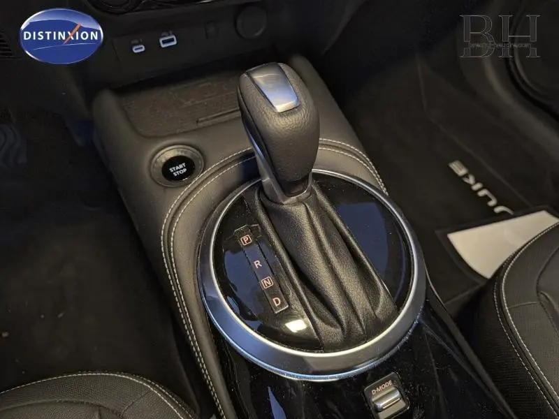 Vue intérieure centrée sur la console centrale du Nissan Juke 1.6 Hybrid 2025, avec cuir noir et tapis marqué Juke.