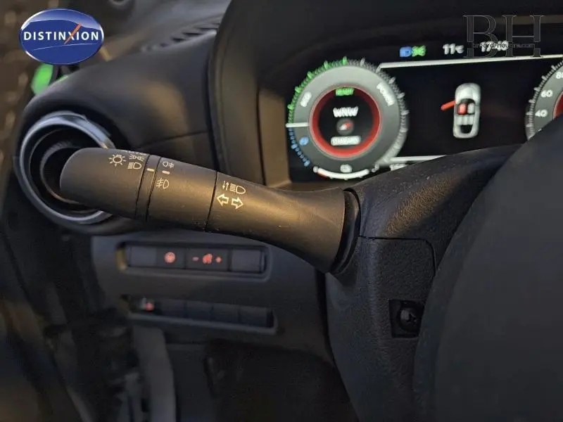 Gros plan sur la commande des phares et clignotants du Nissan Juke 1.6 Hybrid Tekna 2025, tableau de bord numérique en arrière-plan.