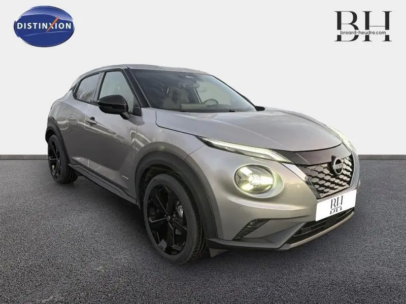 Nissan Juke 1.6 Hybrid Tekna 2025 gris perle métallisé, vue 3/4 avant droit avec phares allumés et jantes noires.