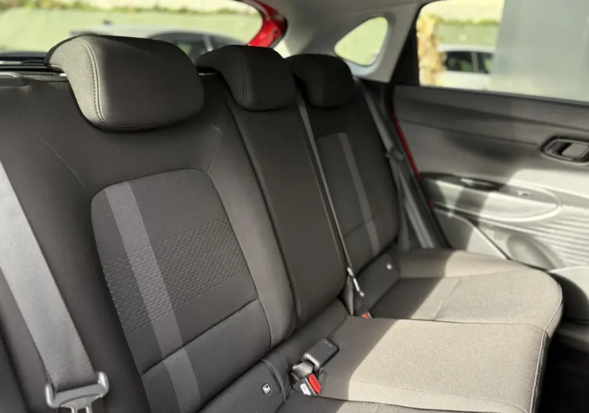 Vue intérieure des sièges arrière noirs de la Hyundai i20 2025, avec ceinture et porte arrière rouge Dragon Metal visible.