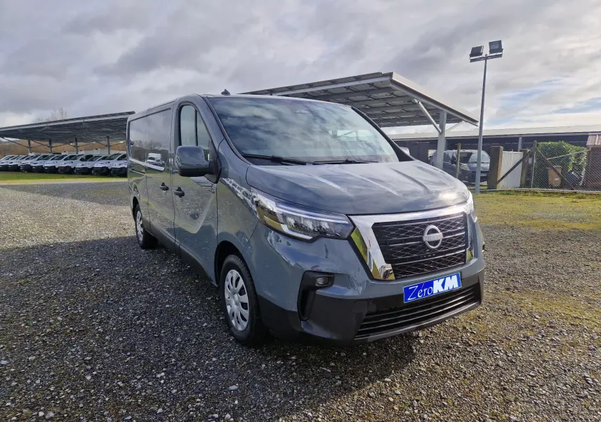 Vue 3/4 avant d’un Nissan Primastar gris urbain 2025 avec calandre chromée et plaque "Zero KM" visible.