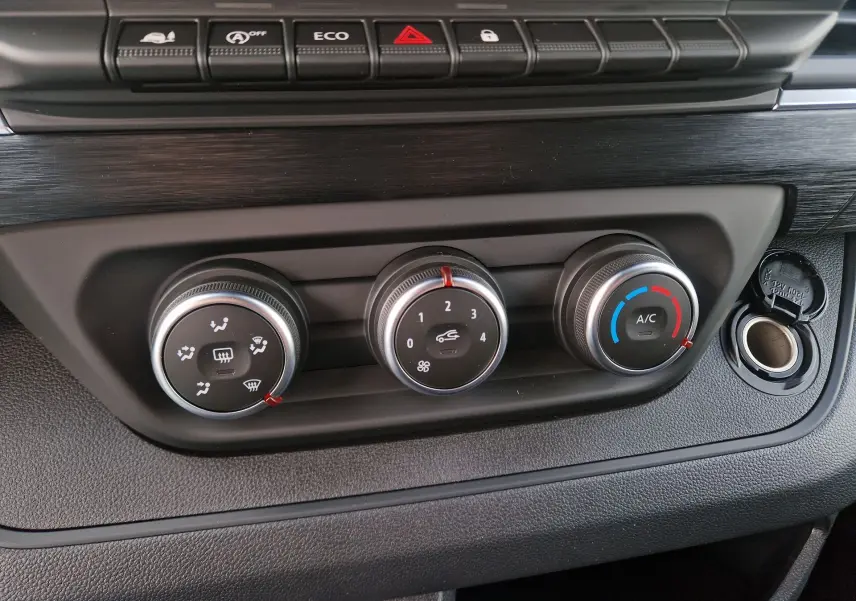 Gros plan sur les commandes de climatisation manuelle et boutons de fonction du tableau de bord du Nissan Primastar gris urbain 2025.