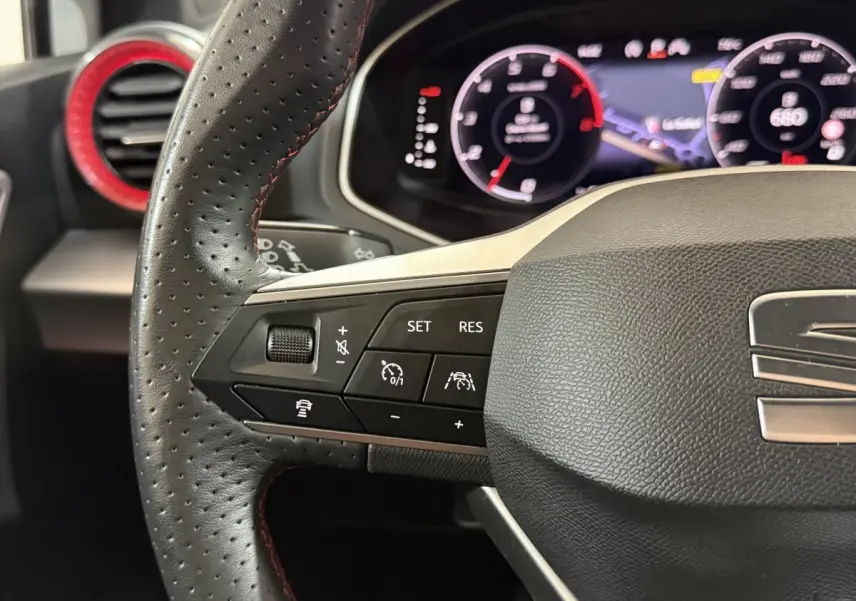 Gros plan sur le volant perforé noir avec surpiqûres rouges de la SEAT Ibiza 2024, tableau de bord numérique en arrière-plan.