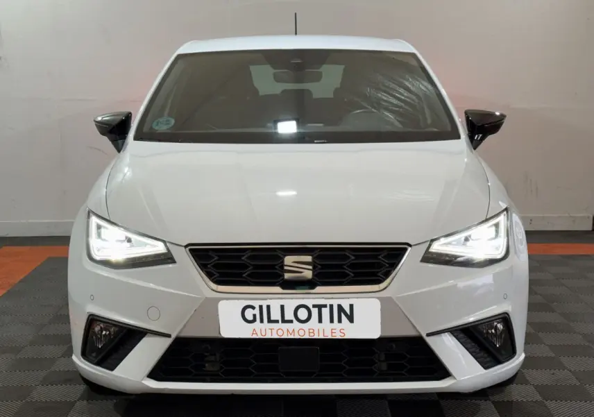 Vue frontale d'une SEAT Ibiza 1.0 TSI 110 FR blanche avec phares LED allumés et calandre hexagonale noire.