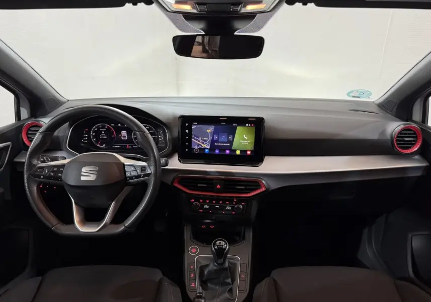 Vue intérieure avant du tableau de bord de la SEAT Ibiza 1.0 TSI 110 FR 2024 avec écran tactile et détails rouges autour des aérateurs.