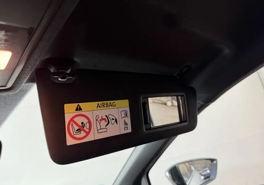 Détail du pare-soleil côté conducteur noir avec miroir intégré et avertissement airbag, rétroviseur extérieur visible.