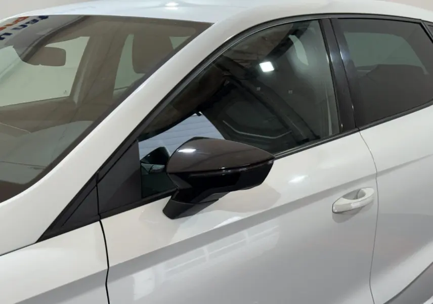 Vue latérale gauche rapprochée d'une SEAT Ibiza blanche 2024 avec rétroviseur noir brillant et poignée de porte intégrée.