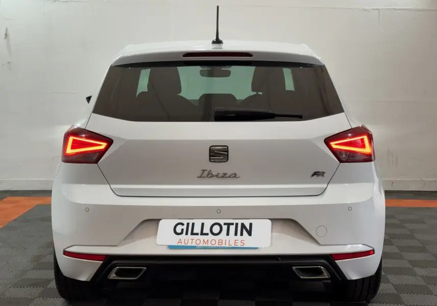 Vue arrière d'une SEAT Ibiza 1.0 TSI 110 FR blanche avec feux LED triangulaires allumés en intérieur.