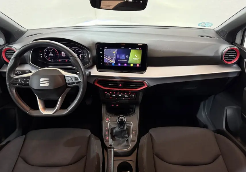 Vue intérieure avant du tableau de bord de la SEAT Ibiza 1.0 TSI 110 FR avec volant cuir, écran tactile et détails rouges.