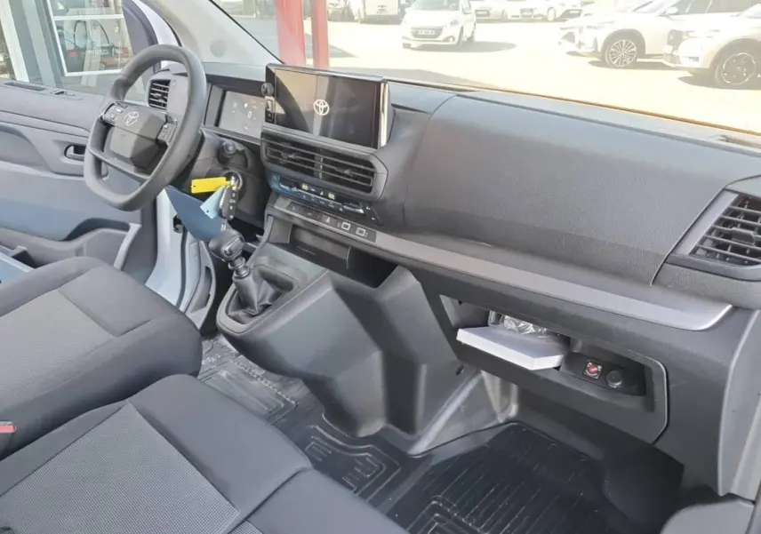 Vue intérieure côté conducteur du Toyota Proace Fourgon blanc Glacier, montrant le tableau de bord et la banquette avant grise.