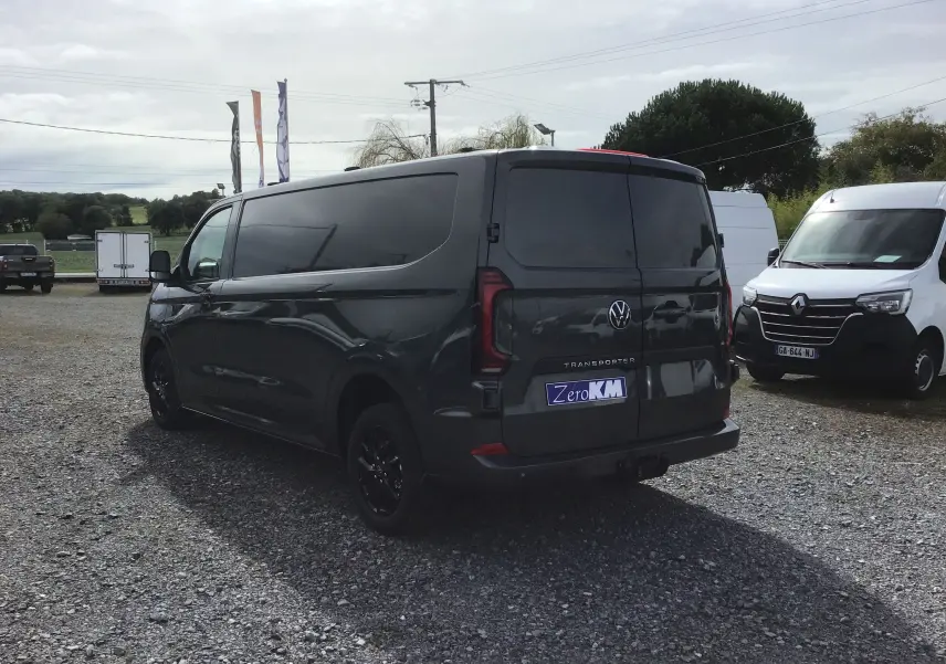 Volkswagen Transporter T7 gris anthracite vu en 3/4 arrière droit, avec barres de toit repliables et jantes noires.