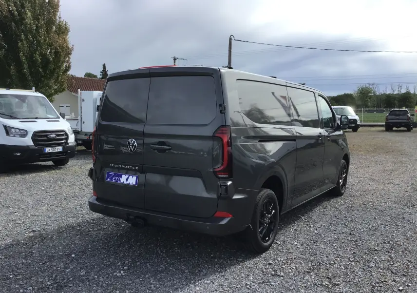 Vue 3/4 arrière droite d'un Volkswagen Transporter gris anthracite avec vitres teintées et jantes noires sur un parking.
