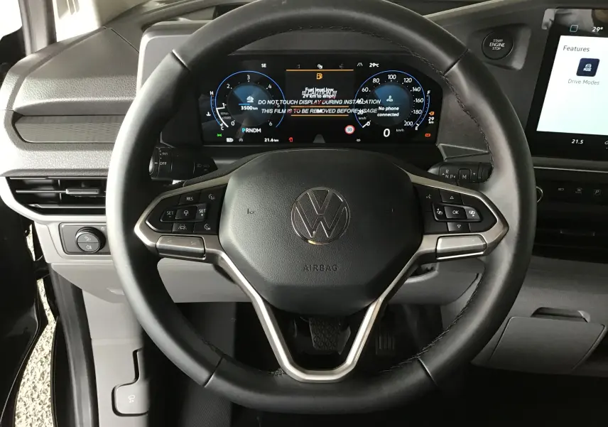 Vue rapprochée du volant multifonctions et du tableau de bord numérique du Volkswagen Transporter T7 gris anthracite, intérieur moderne.