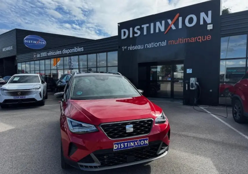 Vue avant d'une SEAT Arona rouge Désir avec toit noir, calandre FR et phares Full LED, devant un concessionnaire Distinxion.
