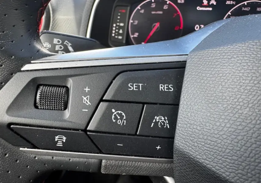Gros plan sur les commandes du volant côté gauche du SEAT Arona 2024 avec surpiqûres rouges et fonctions d’aide à la conduite.