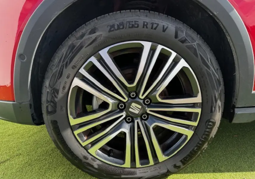 Gros plan sur la jante alliage 17 pouces du SEAT Arona rouge Désir avec logo central sur fond d'herbe verte.