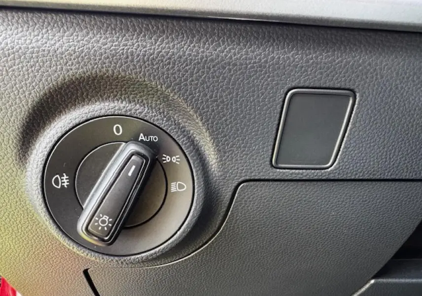 Gros plan sur le bouton de commande des phares dans l'habitacle du SEAT Arona 2024 rouge Désir avec toit noir.