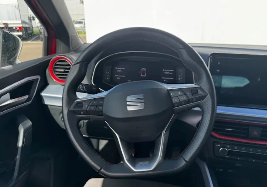 Vue intérieure centrée sur le volant sport en cuir perforé avec surpiqûres rouges du SEAT Arona FR 2024.