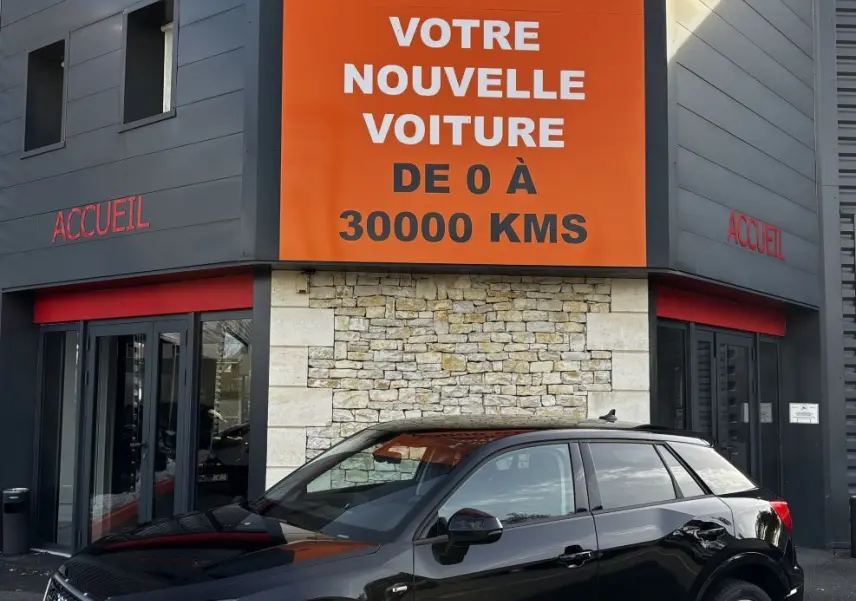 Audi Q2 noir vue 3/4 avant droit, garée devant un bâtiment avec panneau orange Distinxion.