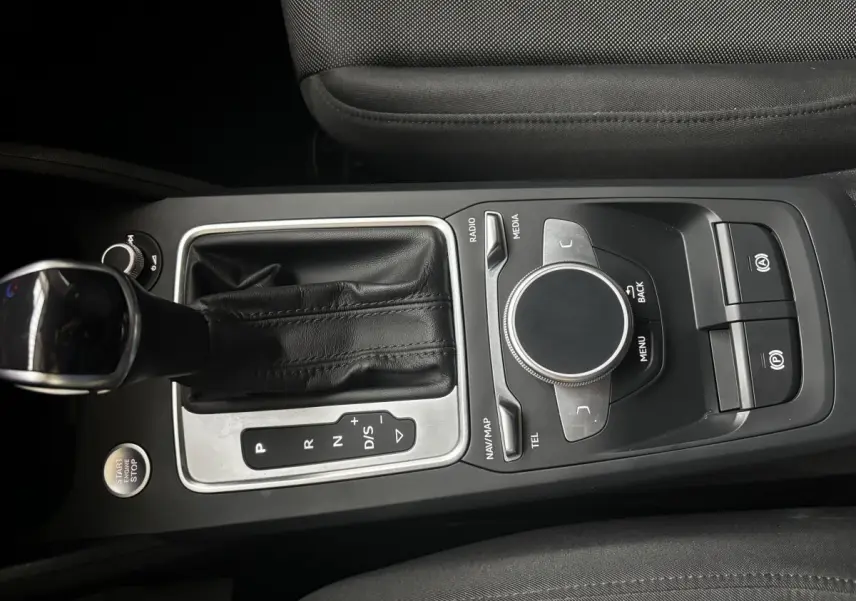 Vue rapprochée de la console centrale noire de l'Audi Q2 35 TFSI 150 S Tronic S Line avec levier de vitesses et commandes multimédia.