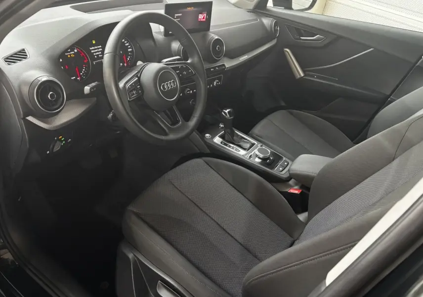 Vue intérieure côté conducteur de l'Audi Q2 noir 35 TFSI S Line 2023, avec tableau de bord digital et volant cuir multifonctions.