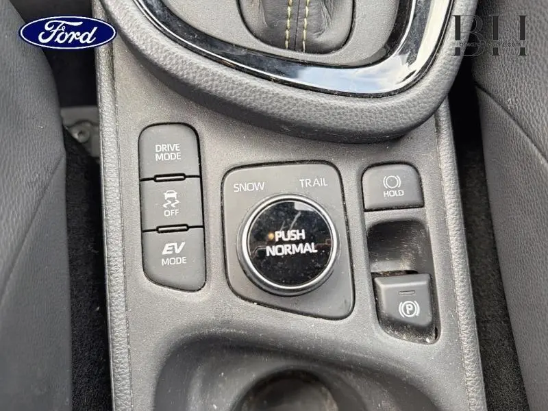 Gros plan sur la console centrale noire avec sélecteur de mode de conduite et boutons de contrôle du frein à main.