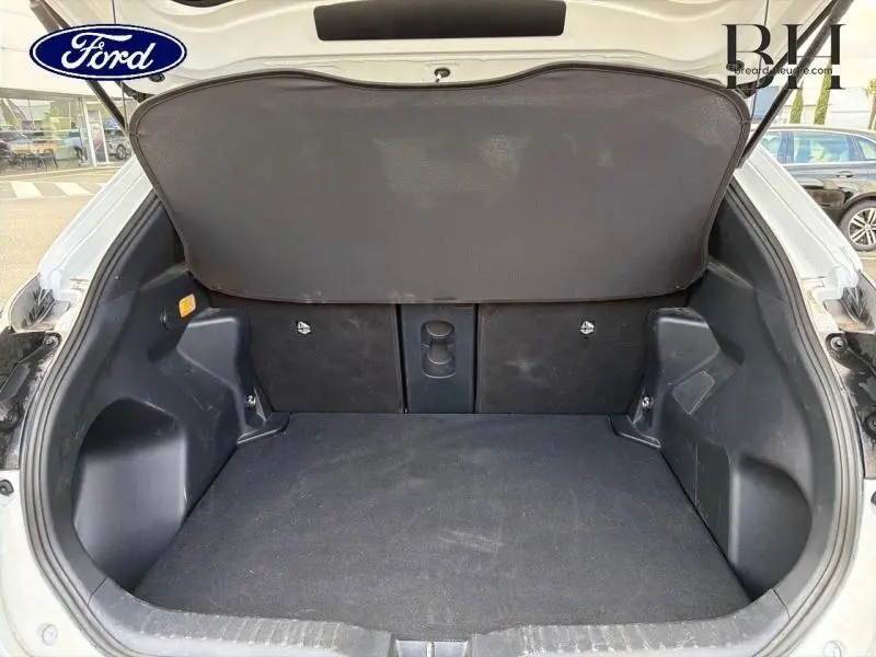 Coffre ouvert vu de l'arrière d'un véhicule blanc, espace de chargement vide avec cache-bagages déployé.