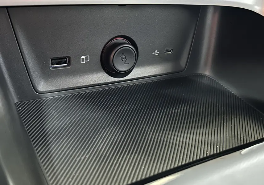Gros plan sur la console centrale du MG ZS Hybrid+ 2025 montrant prises USB, prise 12V et surface texturée noire.