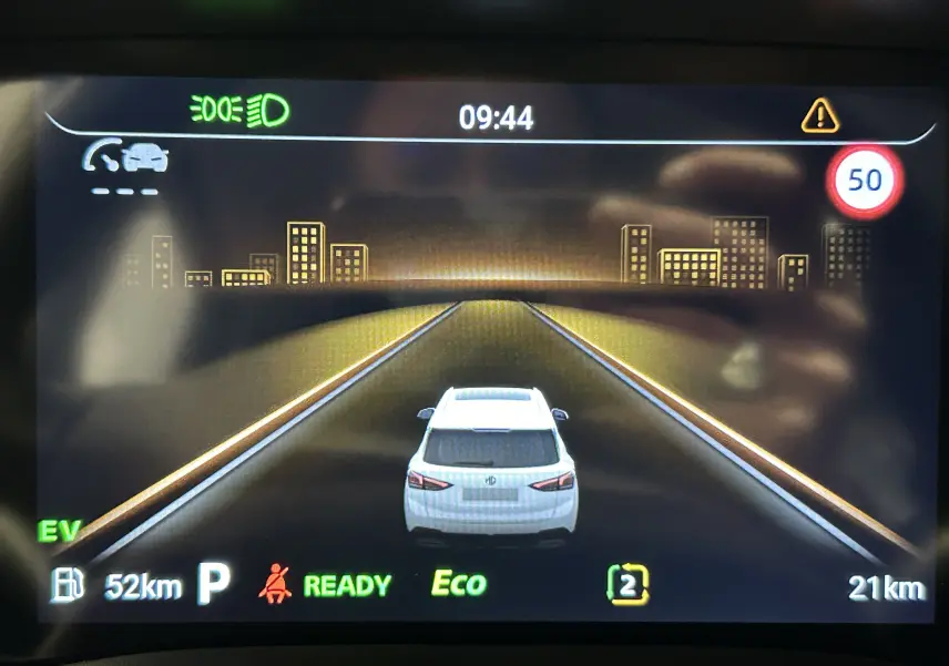 Affichage numérique du tableau de bord montrant une voiture blanche vue de dos sur route virtuelle avec limite à 50 km/h.