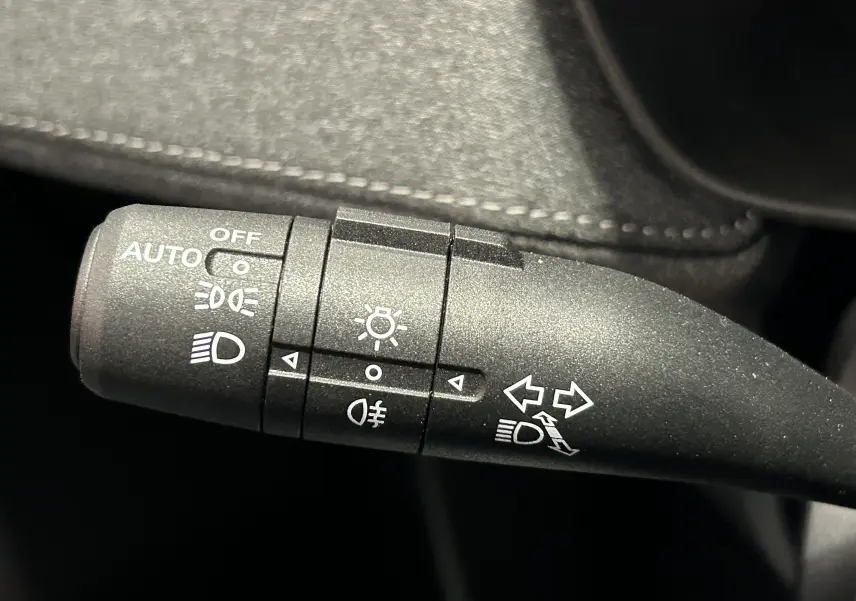 Gros plan sur la commande des phares et clignotants du MG ZS Hybrid+ 2025, avec finition tissu noire visible en arrière-plan.