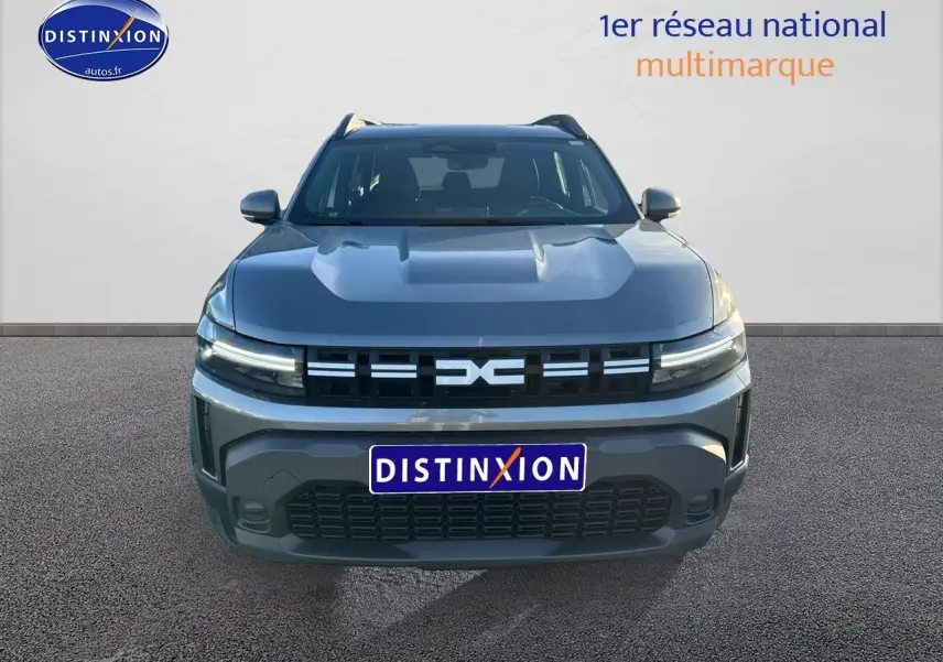 Vue avant d'un Dacia Duster gris schiste 2025 avec calandre distinctive et phares LED allumés.