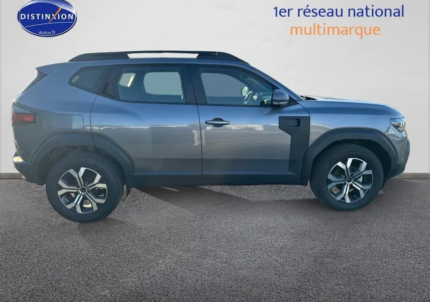 Profil droit du Dacia Duster gris schiste 2025 avec jantes alu et barres de toit visibles.