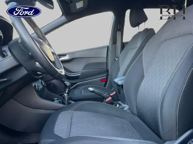 Vue intérieure côté conducteur de la Ford Fiesta 2020, sièges tissu gris avec volant cuir et levier de vitesse manuel.