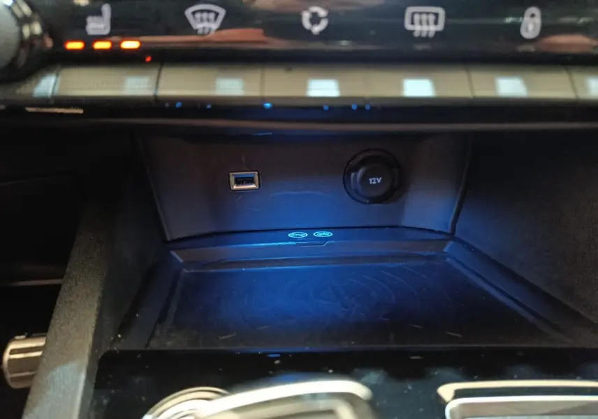 Gros plan sur la console centrale du Peugeot 3008 bleu, avec prise USB, prise 12V et surface de charge sans fil.