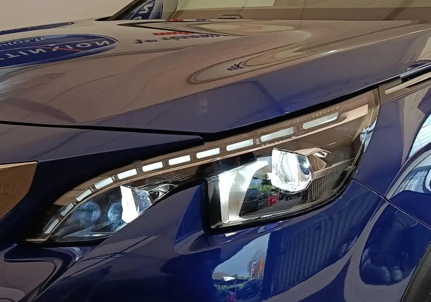Gros plan sur le phare avant droit LED d’un Peugeot 3008 bleu, soulignant les lignes modernes et la finition brillante.