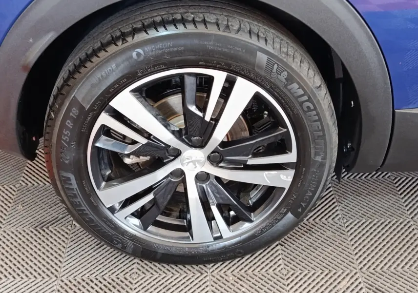 Gros plan sur la roue avant droite d’un Peugeot 3008 bleu, avec jante alliage bicolore et pneu Michelin.