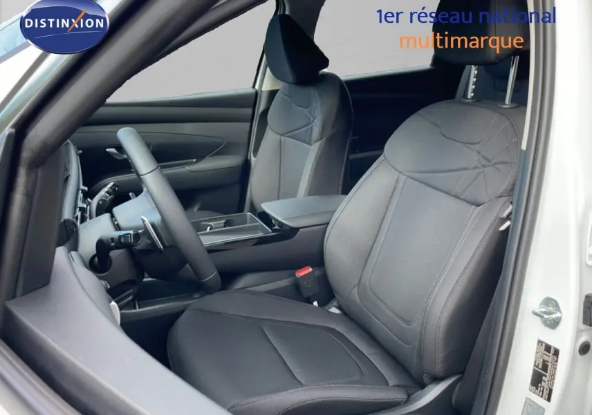 Vue intérieure côté conducteur du Hyundai Tucson blanc Atlas 2026, sièges tissu noir et volant multifonction.