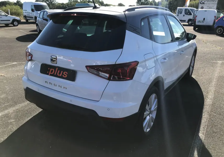 Vue 3/4 arrière droite d'un SEAT Arona blanc avec toit noir, soulignant ses feux arrière et son design compact.
