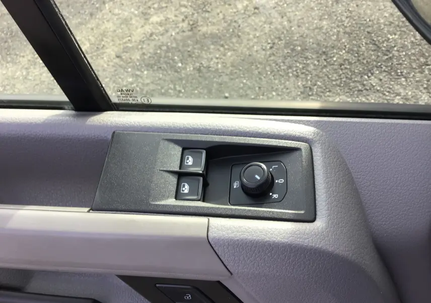 Gros plan sur les commandes de réglage des rétroviseurs et des vitres côté conducteur du Volkswagen Crafter blanc.