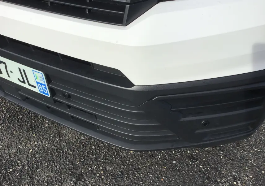 Gros plan sur le pare-chocs avant noir et la calandre du Volkswagen Crafter fourgon blanc, avec plaque d'immatriculation française.