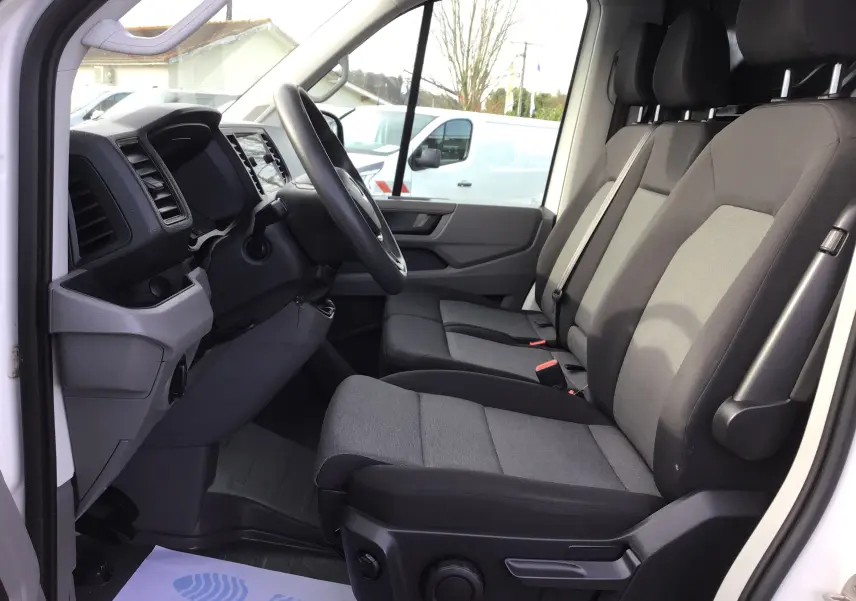 Vue intérieure côté conducteur du Volkswagen Crafter Fourgon blanc 2021, sièges tissu gris et tableau de bord moderne.