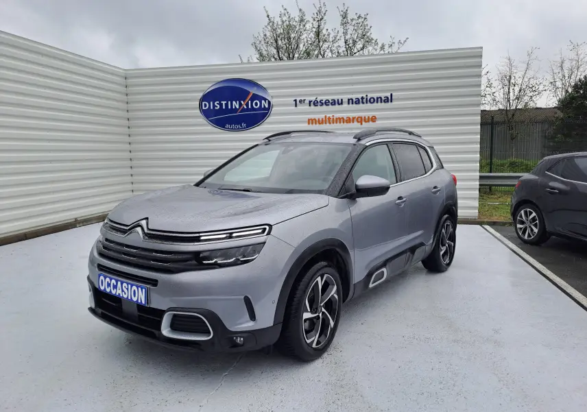 SUV Citroën C5 Aircross gris Artense vu en 3/4 avant droit sous la pluie avec jantes bi-ton et barres de toit.