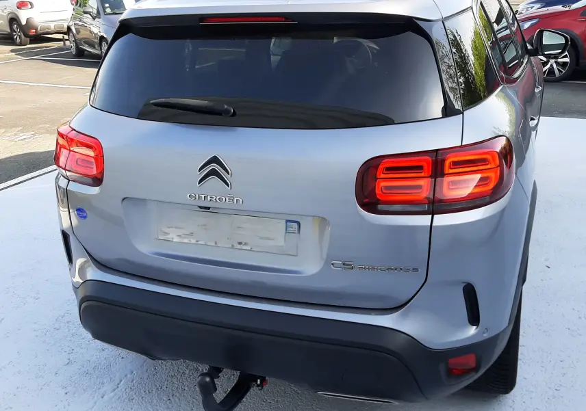 Vue arrière d'un Citroën C5 Aircross gris Artense avec feux allumés et attelage visible sur parking extérieur.