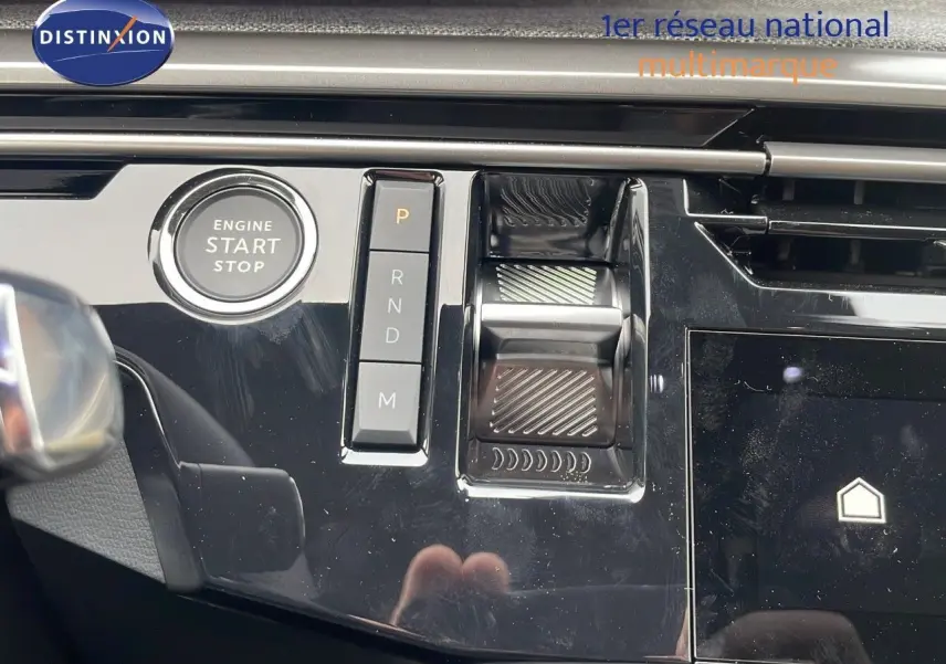 Gros plan sur la console centrale noire brillante du Peugeot 5008 Hybrid 2025 avec bouton start/stop et commandes de boîte auto.