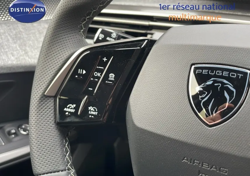 Gros plan sur le volant perforé gris avec commandes intégrées et logo Peugeot du SUV 5008 hybride 2025.