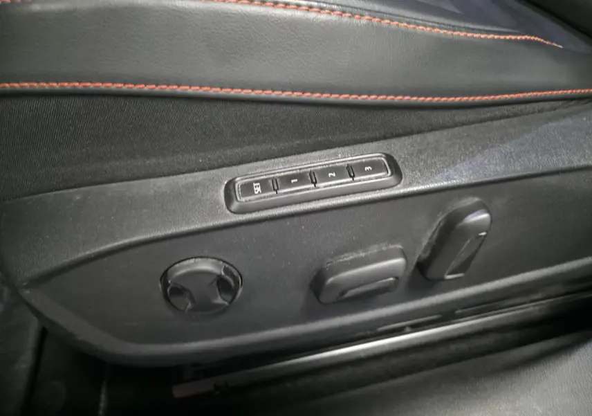 Détail des commandes de réglage électrique du siège conducteur noir avec surpiqûres rouges dans une SEAT Leon Sportstourer gris urbain.