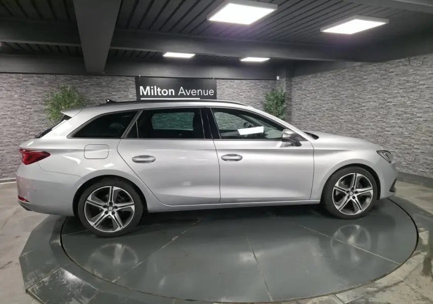 Vue de profil côté gauche d’un break SEAT Leon Sportstourer gris urbain avec jantes alliage et barres de toit chromées.