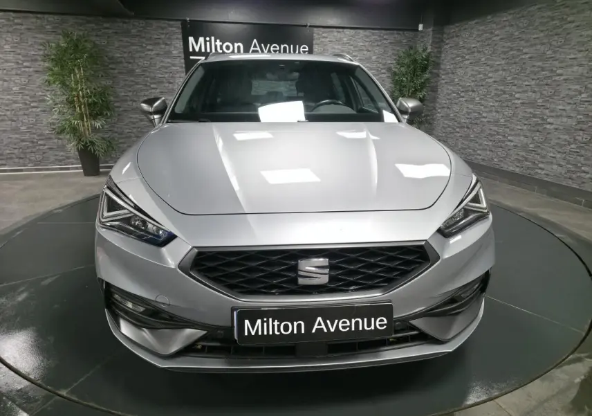 Vue avant d'une SEAT Leon Sportstourer gris urbain avec calandre noire et phares LED anguleux dans un showroom.